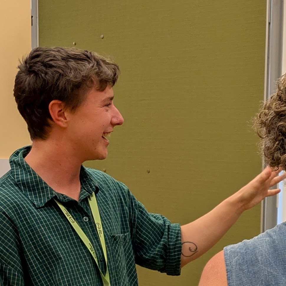 ze pointing at a poster while talking 
           		with someone